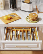 Expandable bamboo utensil organizer neatly storing silverware and kitchen tools inside an open kitchen drawer beneath a modern white countertop.