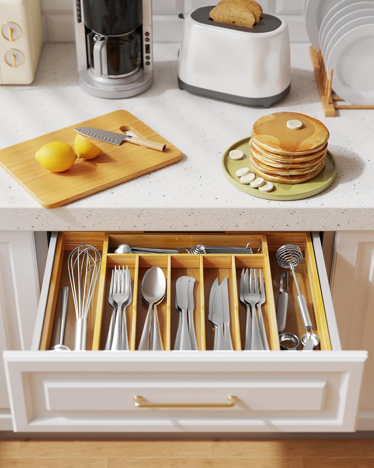 Expandable bamboo utensil organizer neatly storing silverware and kitchen tools inside an open kitchen drawer beneath a modern white countertop.