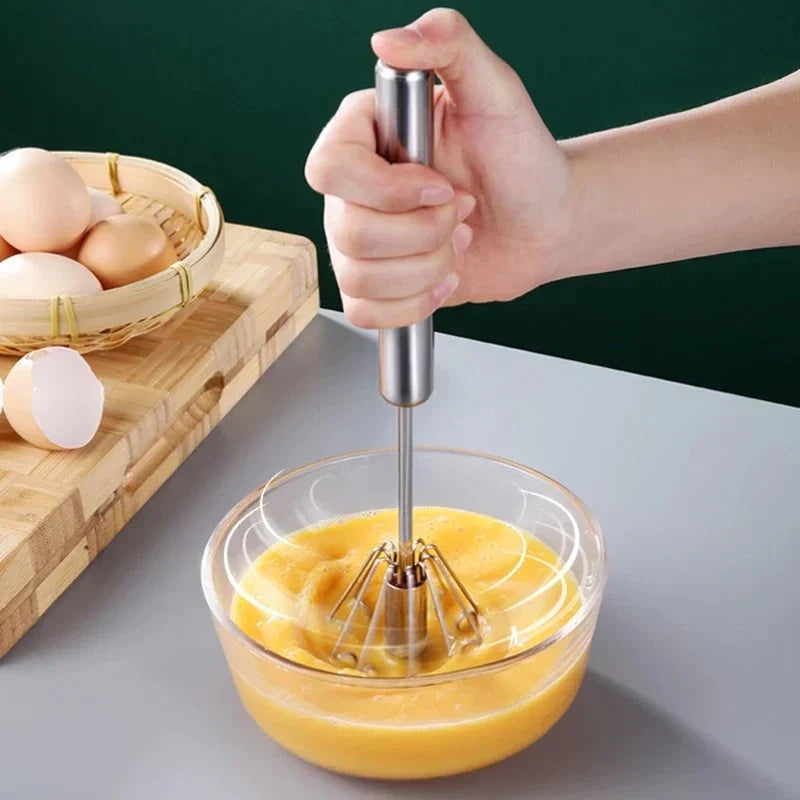 Push-Spin Egg Beater hand whisk shown whipping eggs in a bowl on a kitchen counter